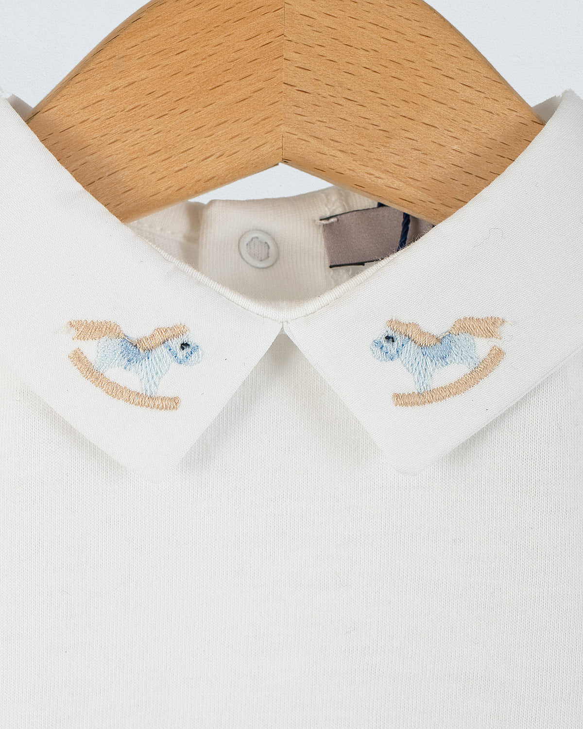 Close-up of the Andreas Baby Onesie’s collar, showing two light blue rocking horse embroideries on each side of the pointed collar.