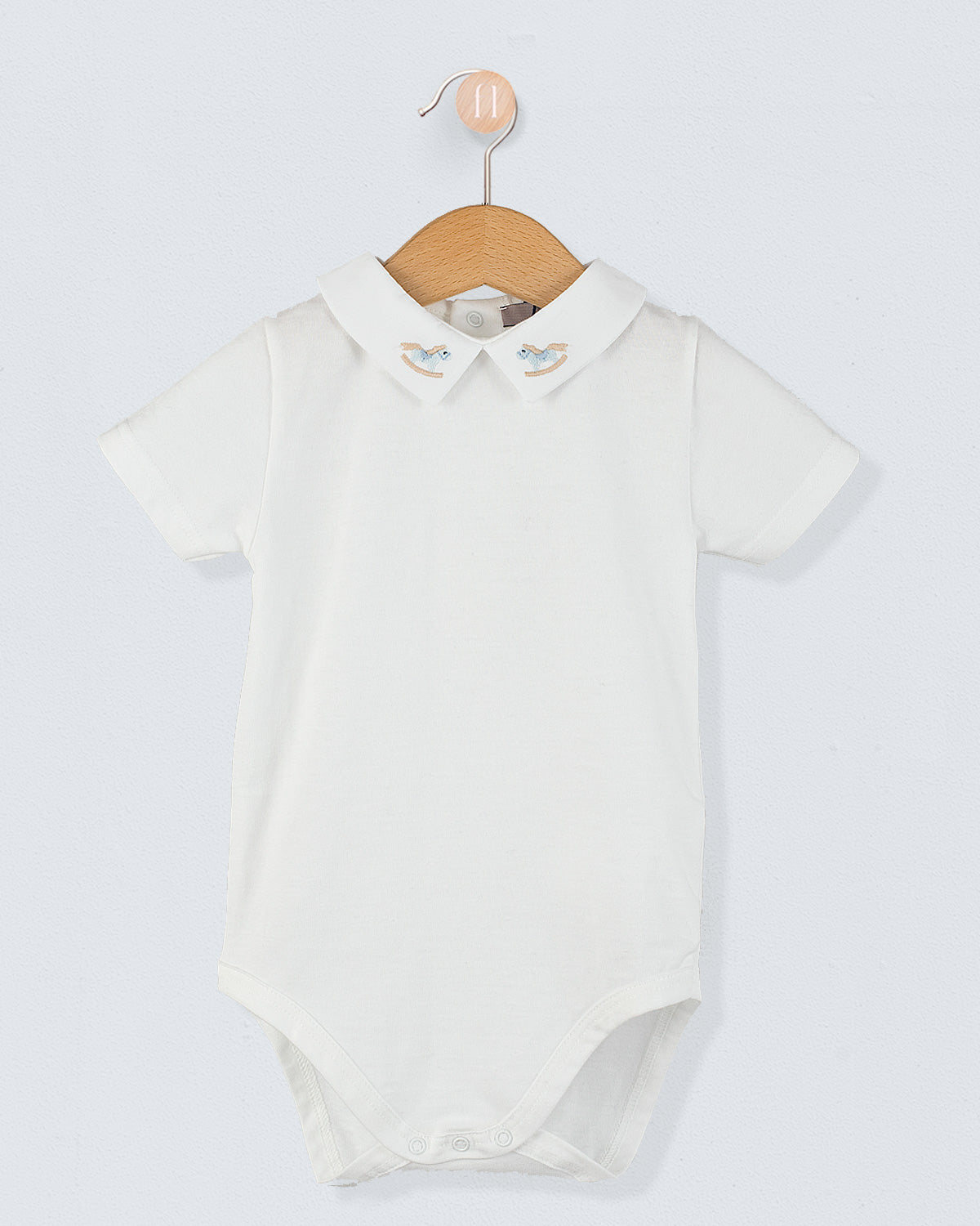 Front view of the Andreas Baby Onesie, a short-sleeve white cotton jersey bodysuit with a pointed collar featuring embroidered light blue rocking horse.