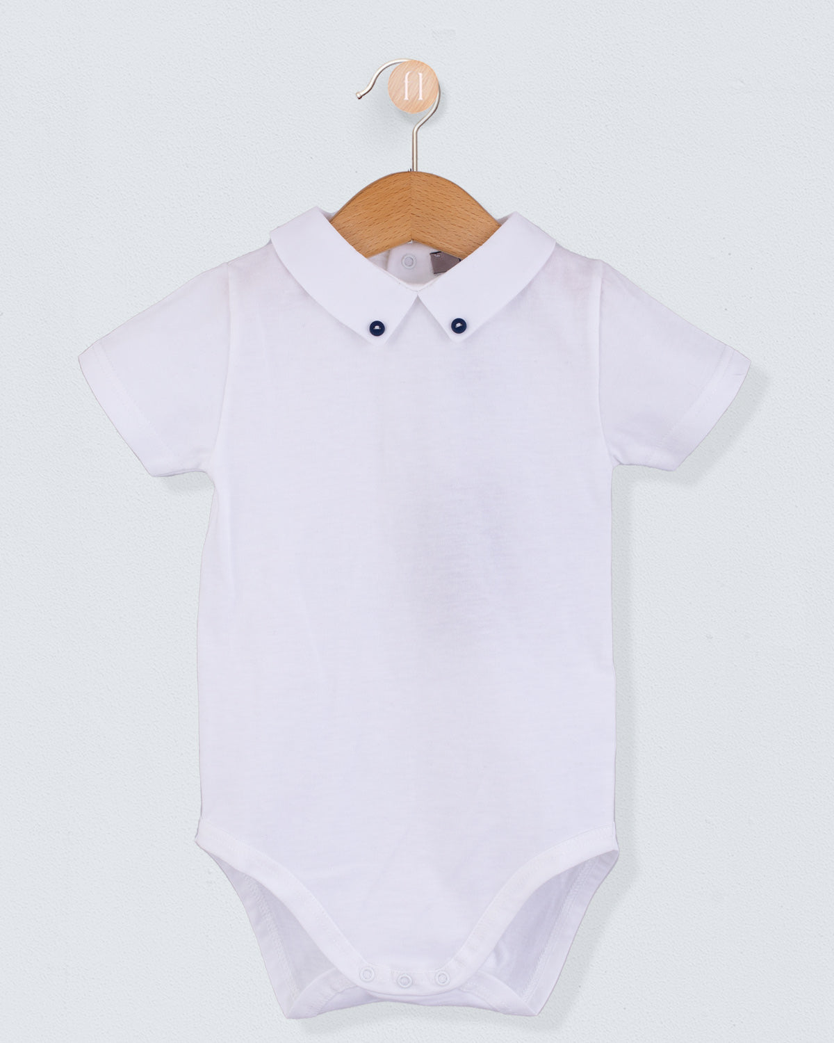 Front view of the Andreas White Onesie with Hunter Buttons, a short-sleeve white cotton jersey onesie with a crisp collar detailed with two small navy buttons.