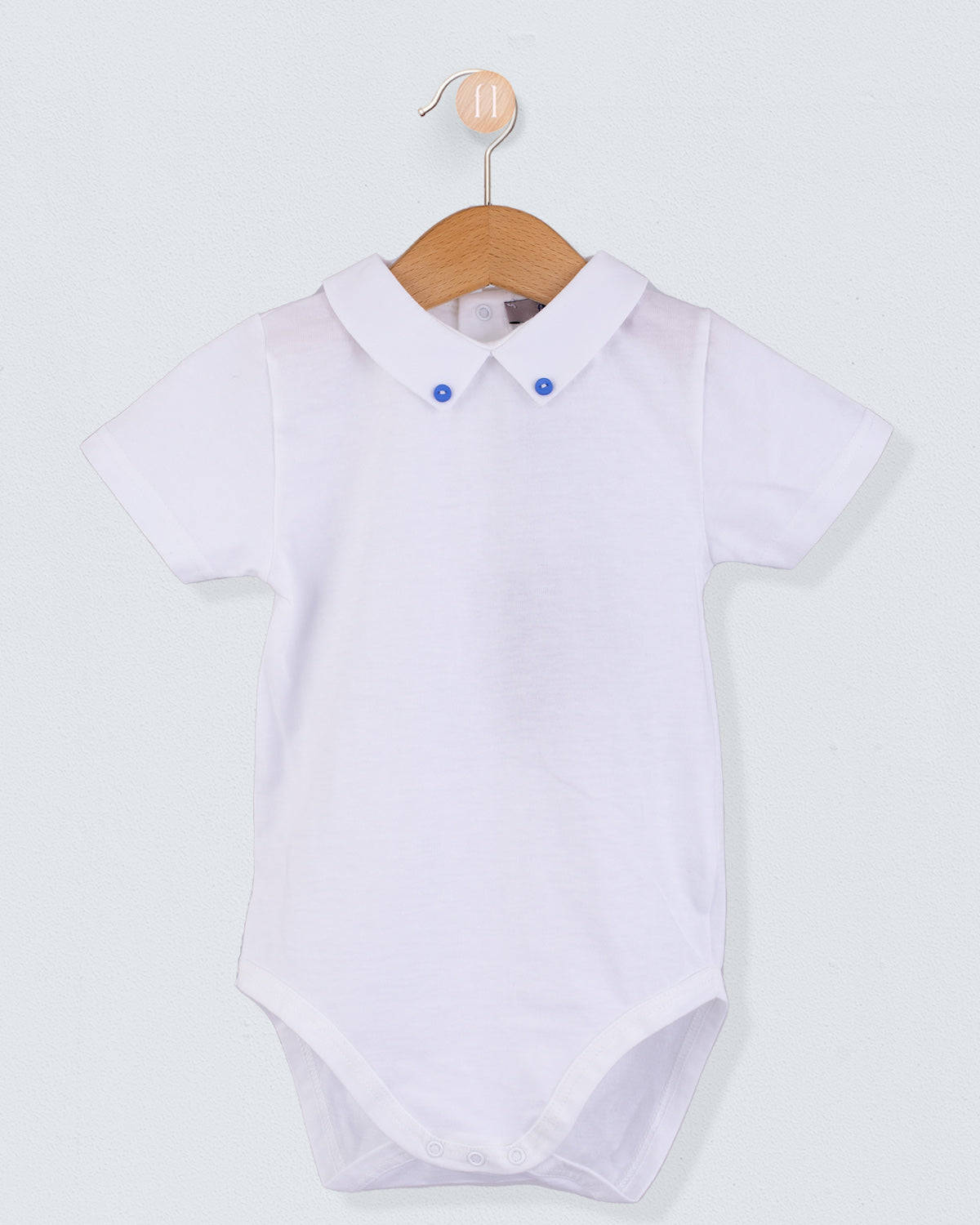 Front view of the Andreas White Onesie with Hunter Buttons, a short-sleeve white cotton jersey onesie with a crisp collar detailed with two small medium blue buttons.