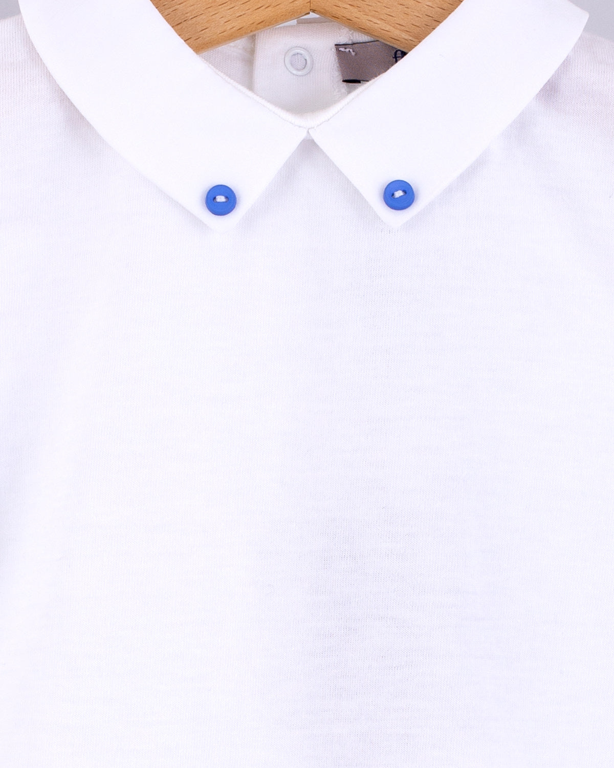 Close-up of the Andreas Onesie collar showing two small medium blue corzo buttons stitched into the tips of the white collar.