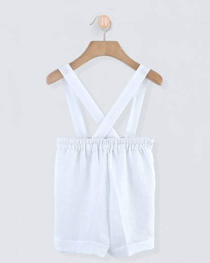 Back view of white linen suspender shorts showing crossed suspenders and gathered waistband, hanging on a wooden hanger