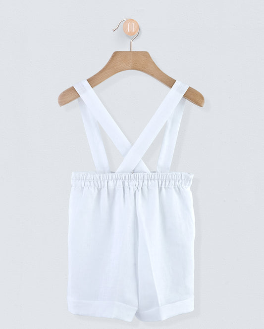 Back view of white linen suspender shorts showing crossed suspenders and gathered waistband, hanging on a wooden hanger
