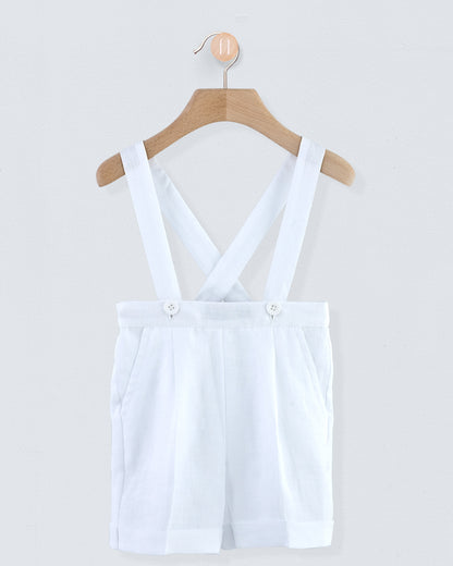 Front view of white linen suspender shorts with corozo buttons, hanging on a wooden hanger