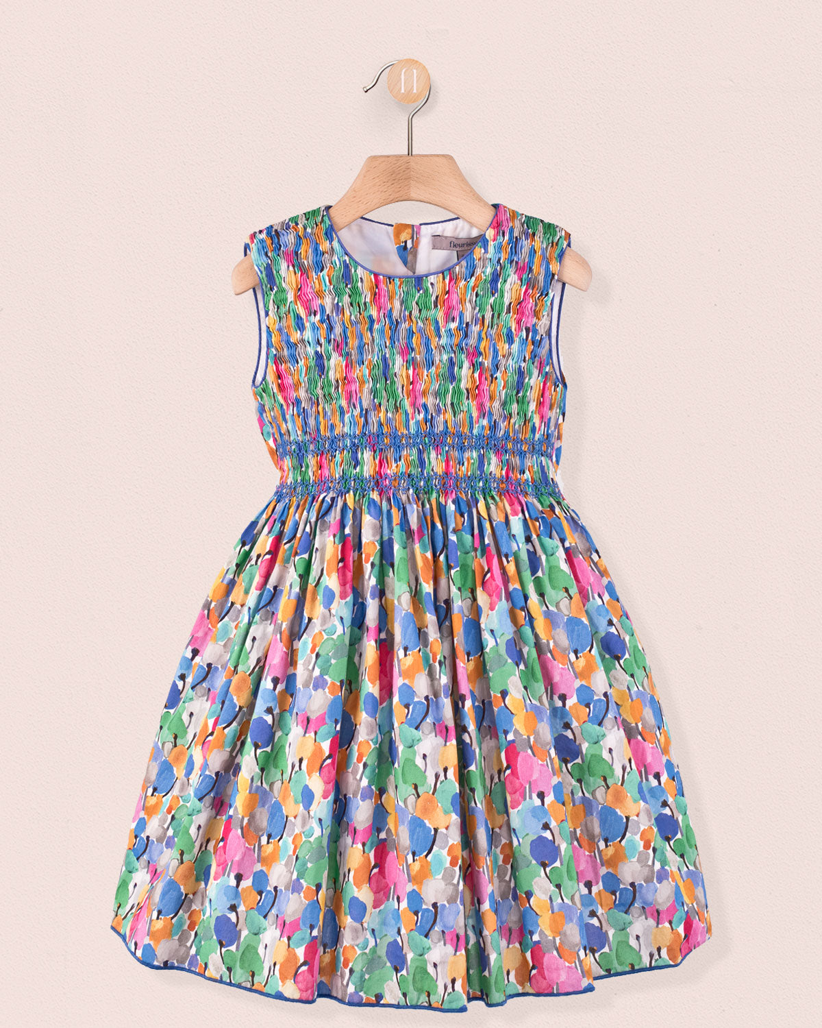 Front view of the Amandine Liberty Tulip Fields Blue Smock dress, a sleeveless cotton dress with a hand-smocked bodice and full skirt in a multicolor tulip Liberty print hanging on a hanger.