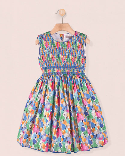 Front view of the Amandine Liberty Tulip Fields Blue Smock dress, a sleeveless cotton dress with a hand-smocked bodice and full skirt in a multicolor tulip Liberty print hanging on a hanger.