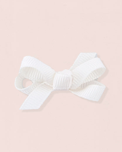 Close-up of a single cream grosgrain baby hairbow attached to velcro, displayed against a light pink 