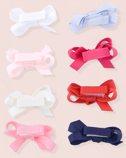 Assortment of grosgrain baby hairbows in various colors including white, light blue, pink, fuchsia, cream, red, rose, and navy blue, arranged flat on a blush pink background.