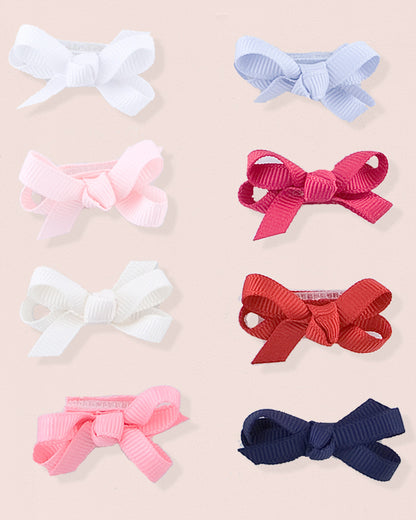 Assortment of grosgrain baby hairbows in various colors including white, light blue, pink, primrose, cream, red, fuchsia, and navy blue, arranged flat on a blush pink background.