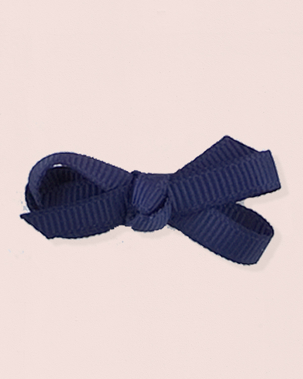 Close-up of a single navy grosgrain baby hairbow attached to velcro, displayed against a light pink 