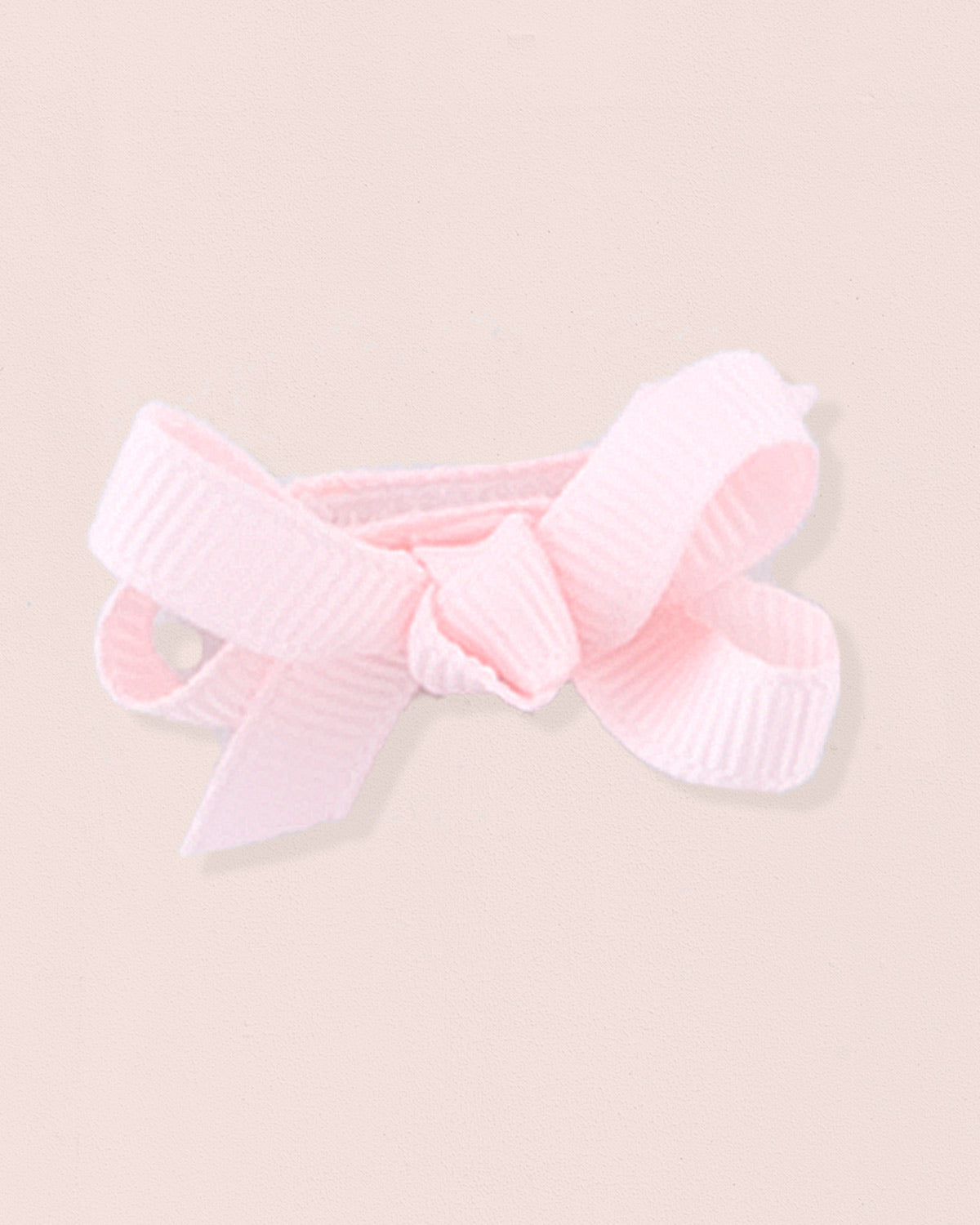 Close-up of a single pink grosgrain baby hairbow attached to velcro, displayed against a light pink 