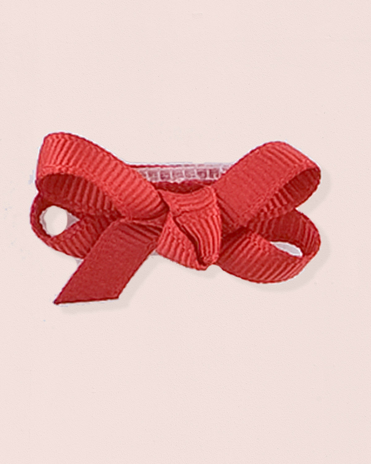 Close-up of a single red grosgrain baby hairbow attached to velcro, displayed against a light pink 