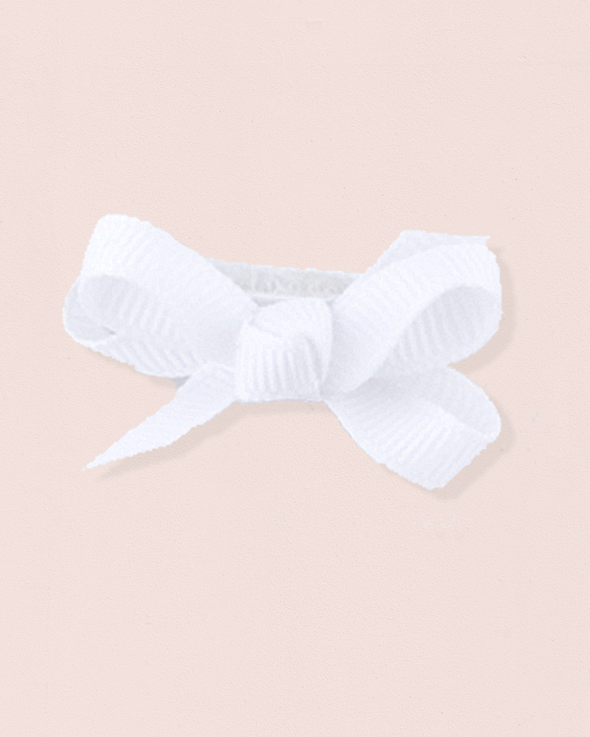 Close-up of a single white grosgrain baby hairbow attached to velcro, displayed against a light pink 