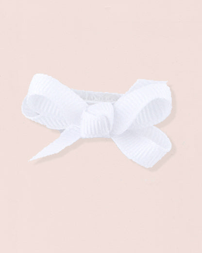 Close-up of a single white grosgrain baby hairbow attached to velcro, displayed against a light pink 