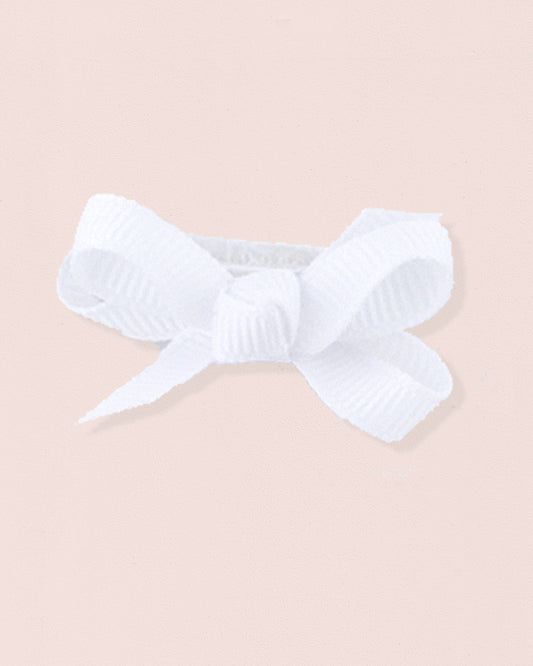 Close-up of a single white grosgrain baby hairbow attached to velcro, displayed against a light pink 
